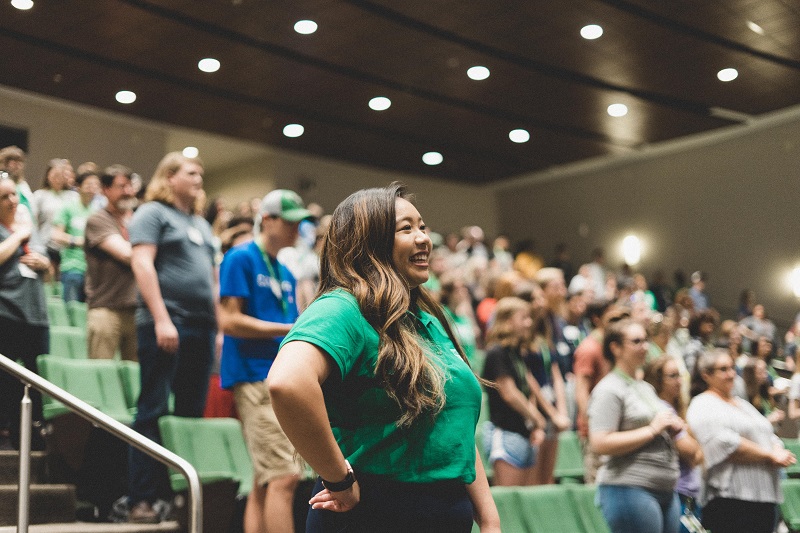 A girl wearing UNT Logo shirt standing along with the other audience in the stadium